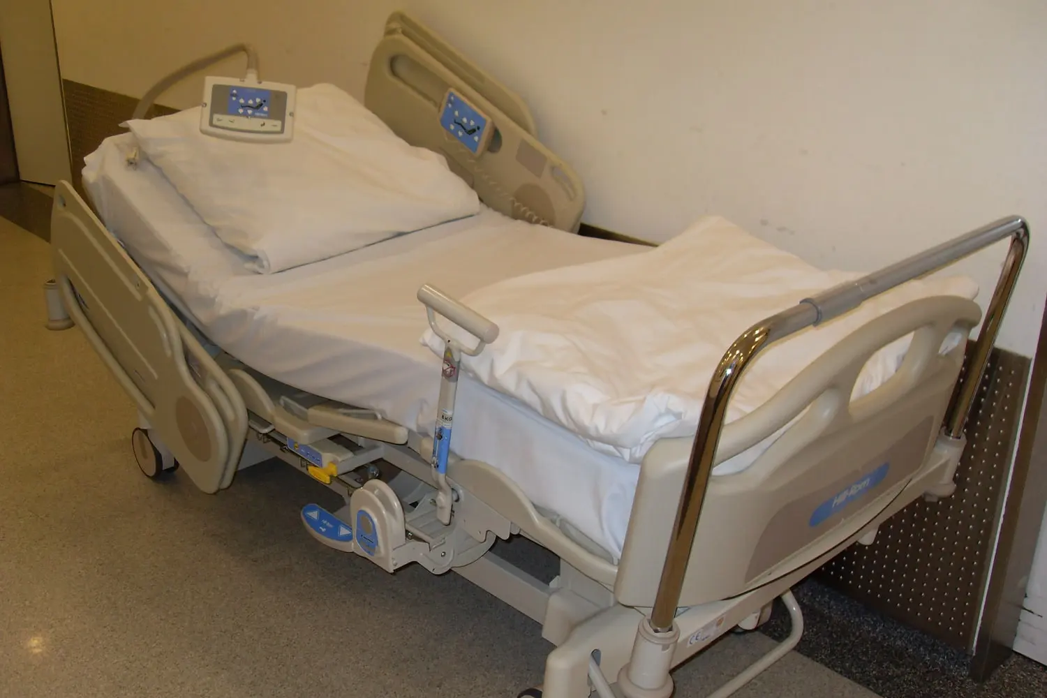 Cama hospitalar com grades laterais levantadas, colchão e rodízios, vista de lado