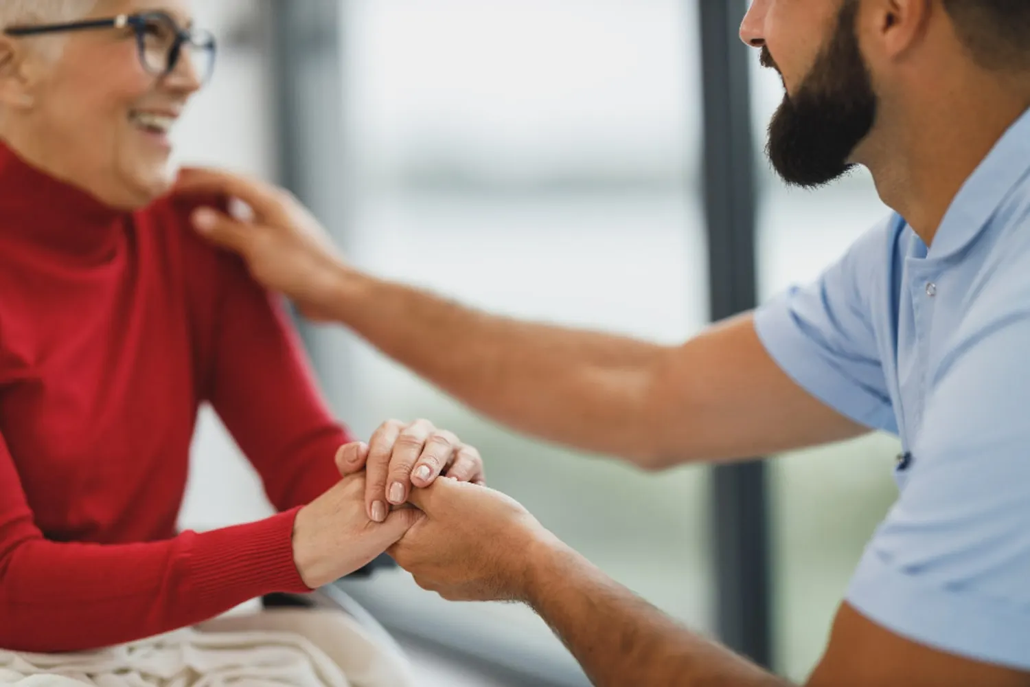 Cuidador segurando as mãos de uma senhora durante o atendimento em casa